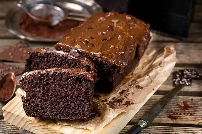 Um bolo de chocolate pequeno e duas partes dele á frente cortadas, em uma tábua de madeira