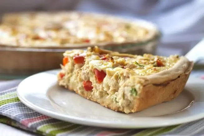 Um pedaço triangular de torta de frango á frente em um prato branco e ao fundo em uma travessa o restante da torta