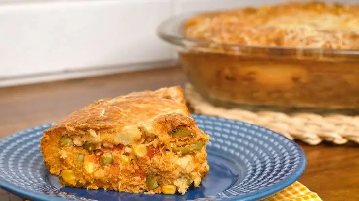 Um pedaço triangular de torta de frango em um prato azul e ao fundo o resto da torta