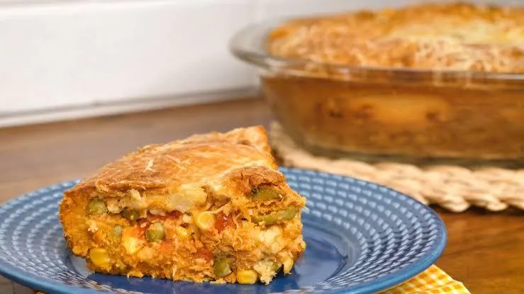 Um pedaço triangular de torta de frango em um prato azul e ao fundo o resto da torta