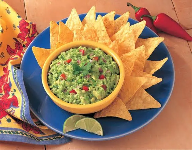 Um pote amarelo com guacamole dentro e em volta nachos organizados um em cima do outro