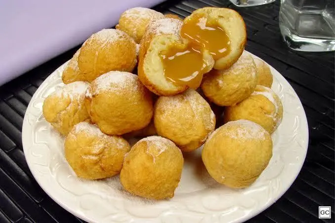 Bolinhos de chuva em cima de um prato branco em que um deles está partido do meio mostrando o recheio de doce de leite