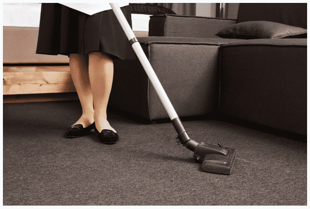 Retrato recortado de mulher em uniforme de empregada, limpando o chão com aspirador