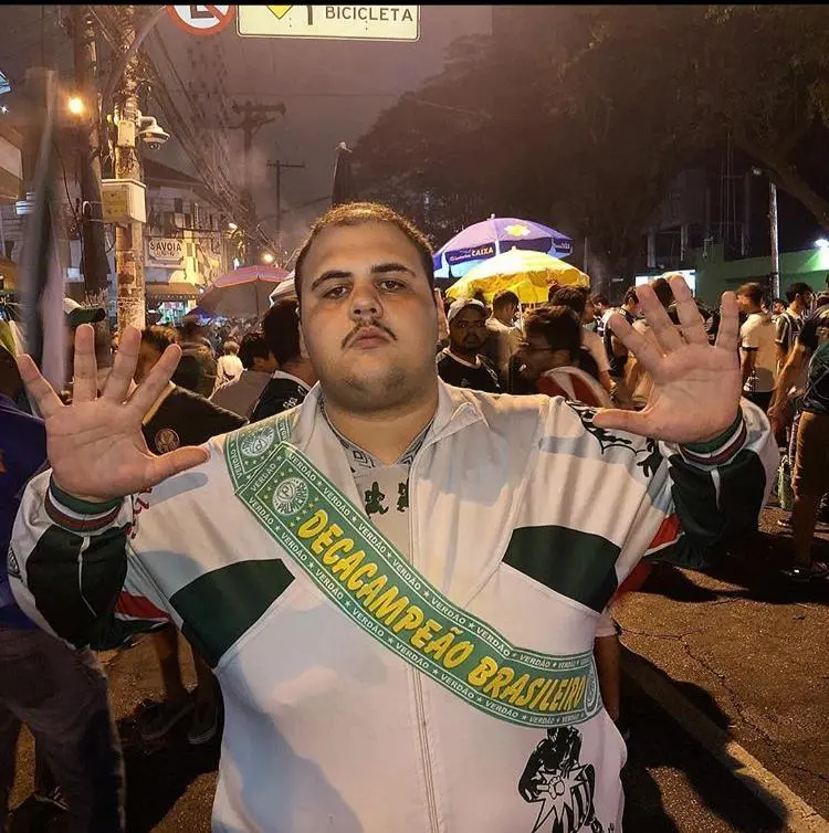 Giovanni Tomoatti torcedor palmeirense na rua fazendo o sinal de 10 coma mão, no peito uma faixa escrito "Decacampeão brasileiro"