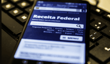 Celular com site da receita federal aberto, em cima de um teclado.