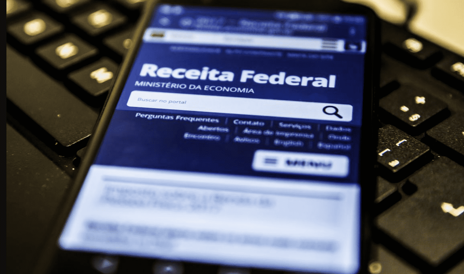 Celular com site da receita federal aberto, em cima de um teclado.