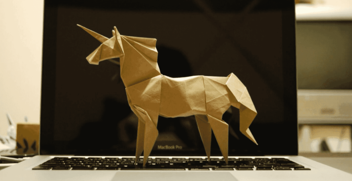 Imagem mostra um unicórnio feito de papelão, de lado e em cima de um notebook aberto.