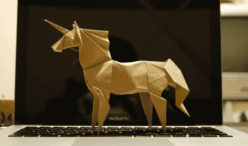 Imagem mostra um unicórnio feito de papelão, de lado e em cima de um notebook aberto.
