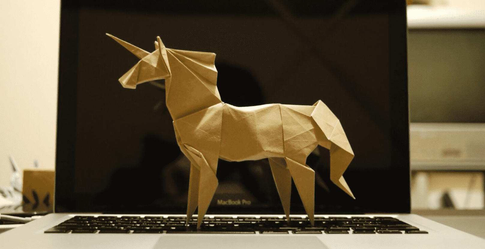 Imagem mostra um unicórnio feito de papelão, de lado e em cima de um notebook aberto.