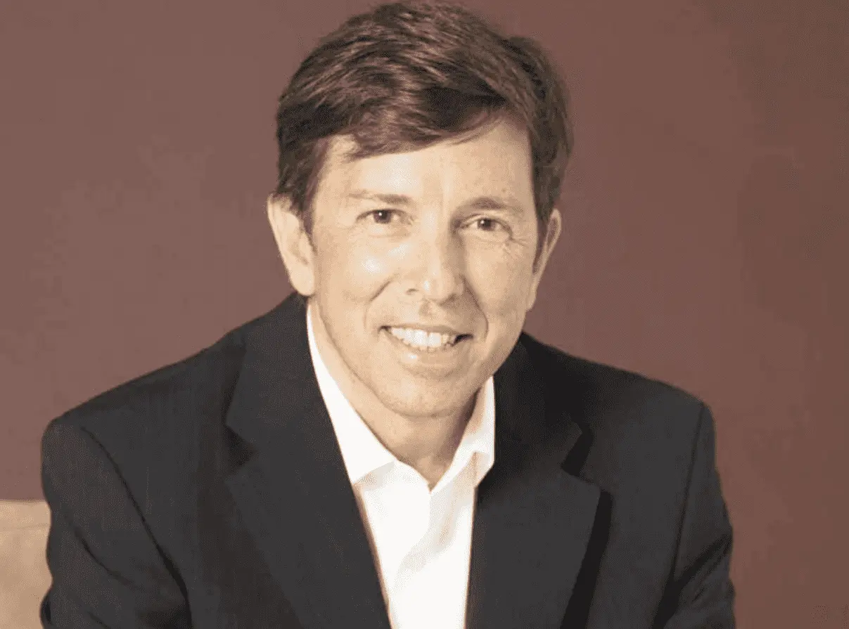 Foto mostra João Amoedo, do tronco para cima, sorrindo para câmera. 