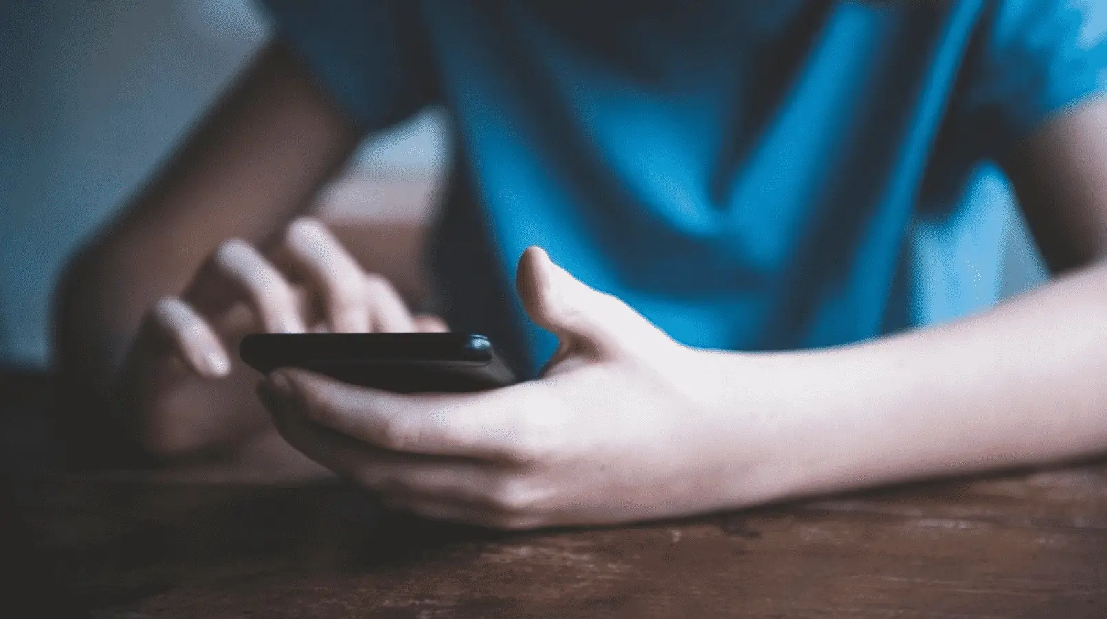 Imagem mostra pessoa apoiada em uma mesa com o celular em mãos.