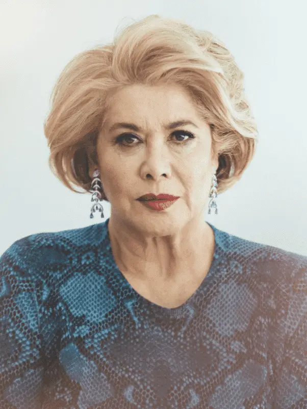 Foto da ex-milionária Patricia Kluge, mulher idosa, loira, usando brincos e um vestido azul. 