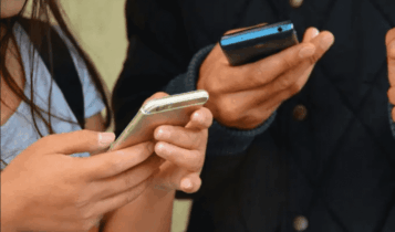 Foto mostra duas pessoas segurando celular nas mãos.