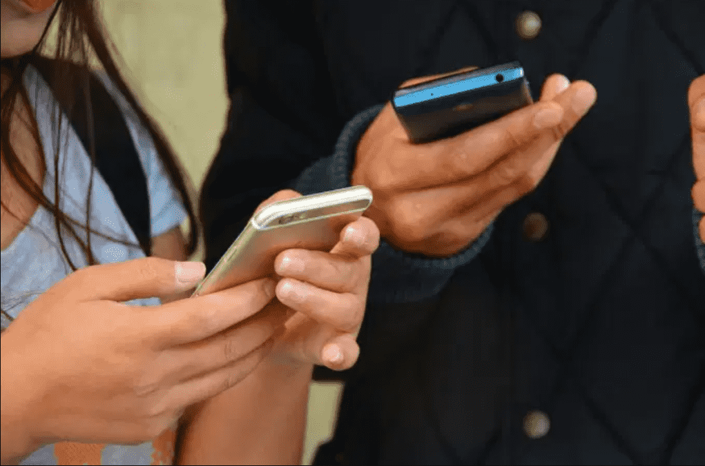 Foto mostra duas pessoas segurando celular nas mãos.