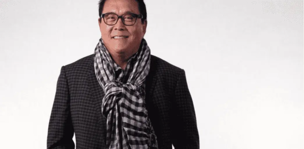 Foto mostra um home adulto em pé, usando paletó e um cachecol xadrez