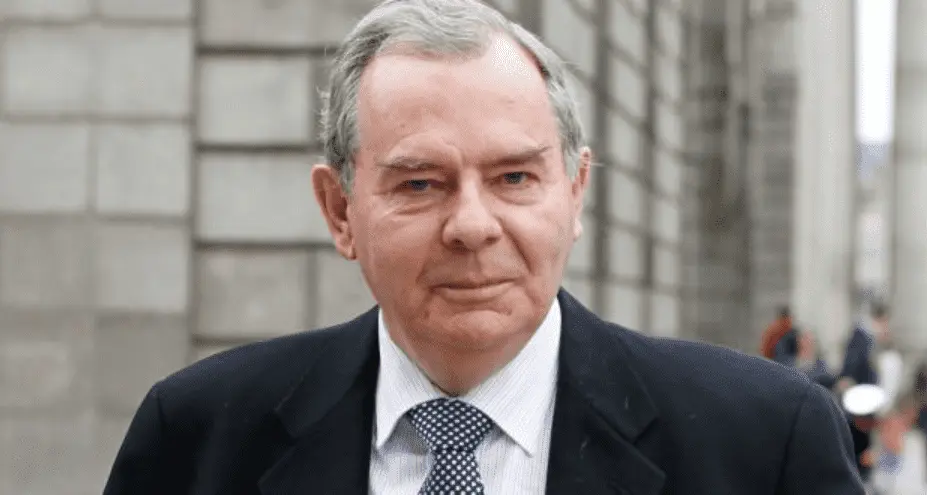 Foto de um homem idoso, com cabelos grisalhos e vestindo um terno. 