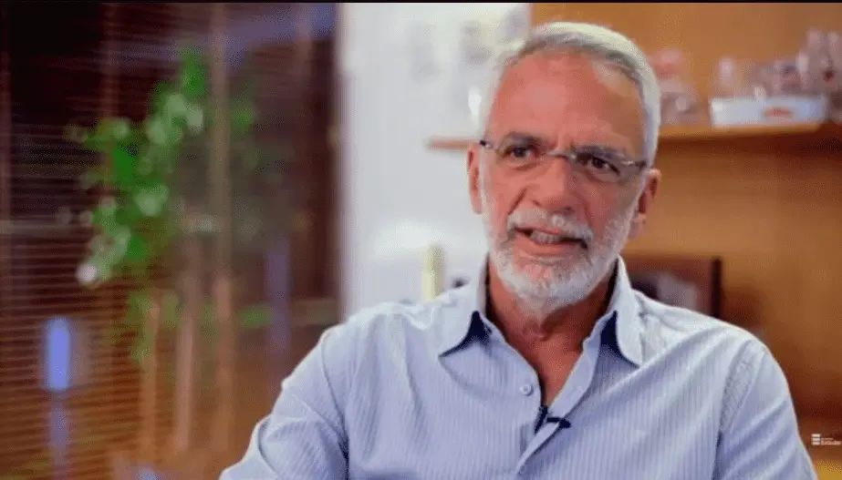 Homem, com cabelos e barba brancos, de camisa social. 