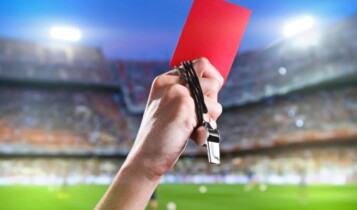 "Pra cego ver": na foto ilustrativa temos um foto não-verbal com um braço com um cartão vermelho à mão para jogadores suspensos