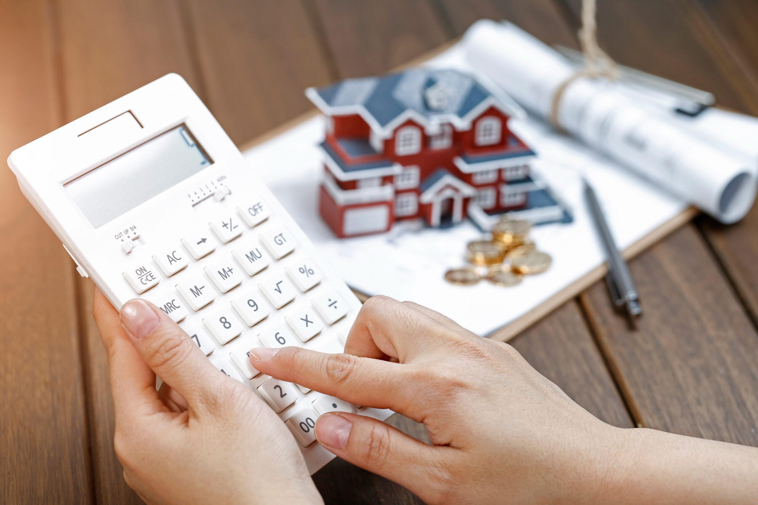 Fundos imobiliários. Pessoa com calculadora e casa de brinquedo ao fundo
