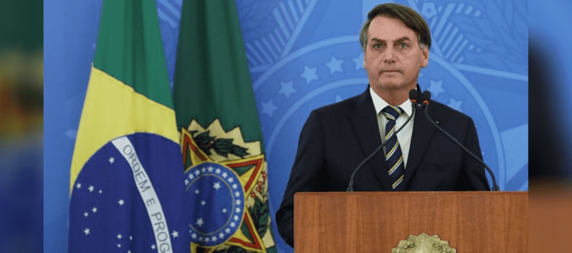 Conheça a lei de negociação de dívidas das micro empresas: Jair Bolsonaro aparece em púlpito à frente de fundo azul com o brasão Federal