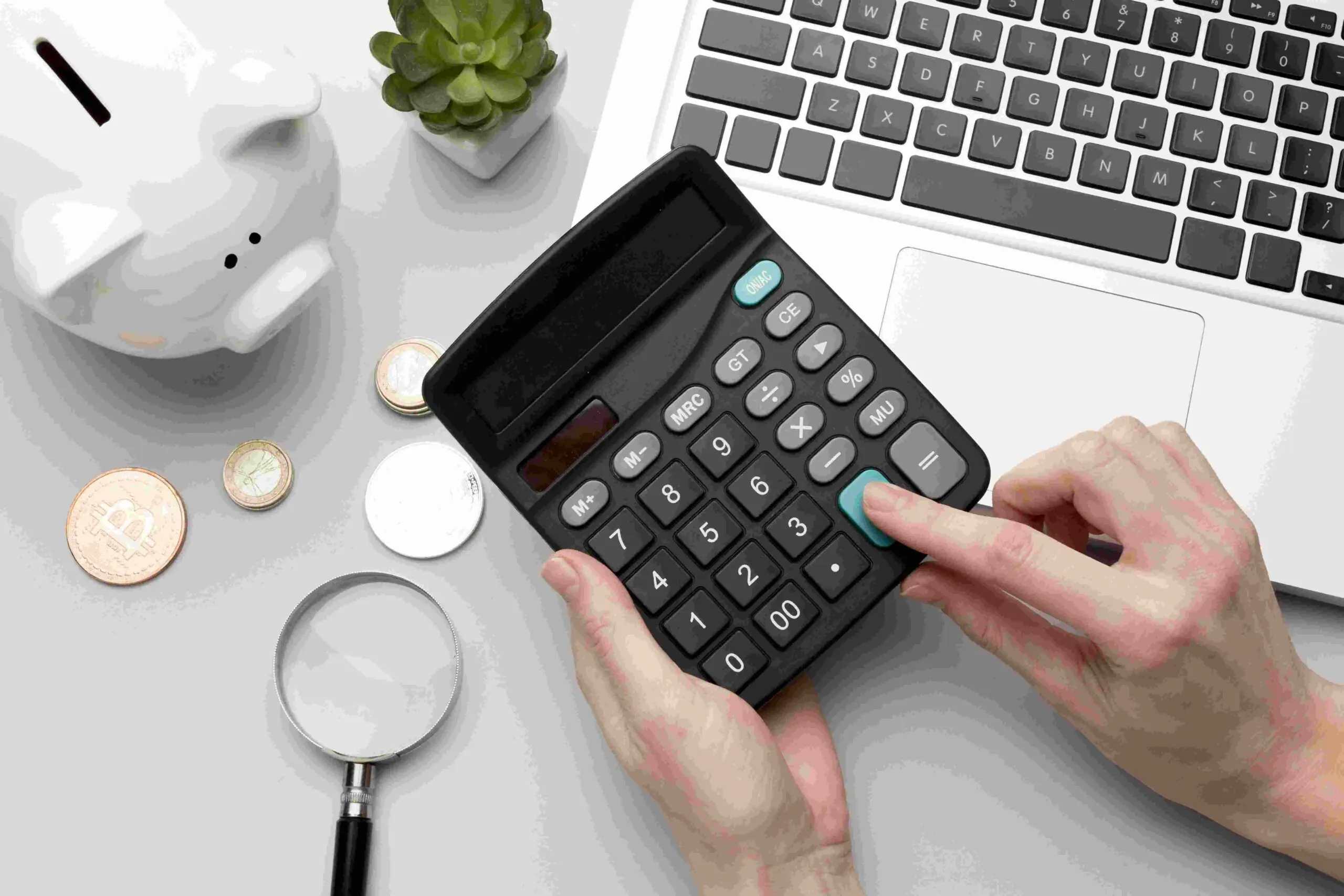 Reserva de emergência. Pessoa usando a calculadora, na cena há moedas, um cofrinho e um notebook.