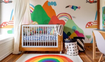 berço de bebê com roupa de cama colorida em frente a um papel de parede colorido de montanhas e passados.