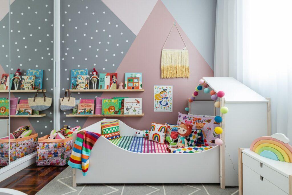 Cama casinha com lençóis coloridos, luminária de bolinhas com livros infantis na parede