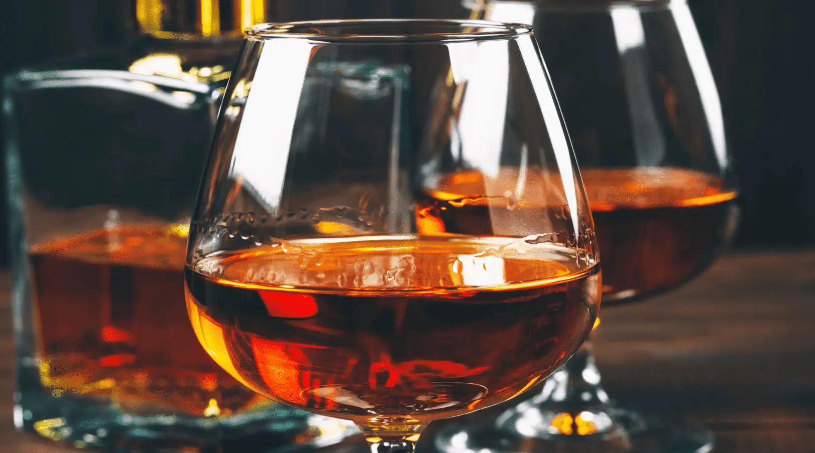 Foto mostra três copos com conhaque.