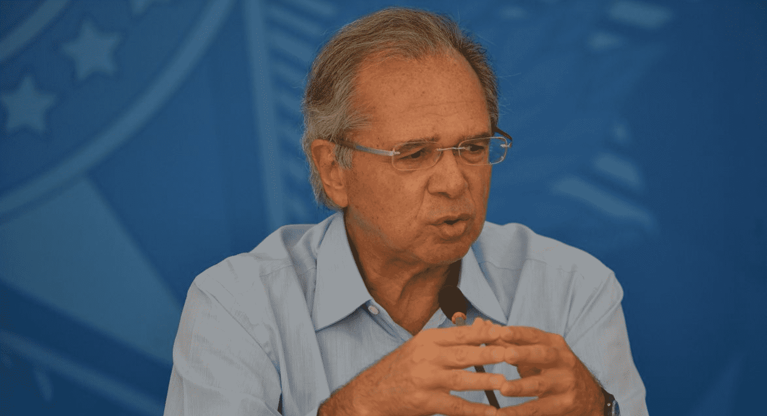 Foto mostra Paulo Guedes falando em um microfone. imposto digital