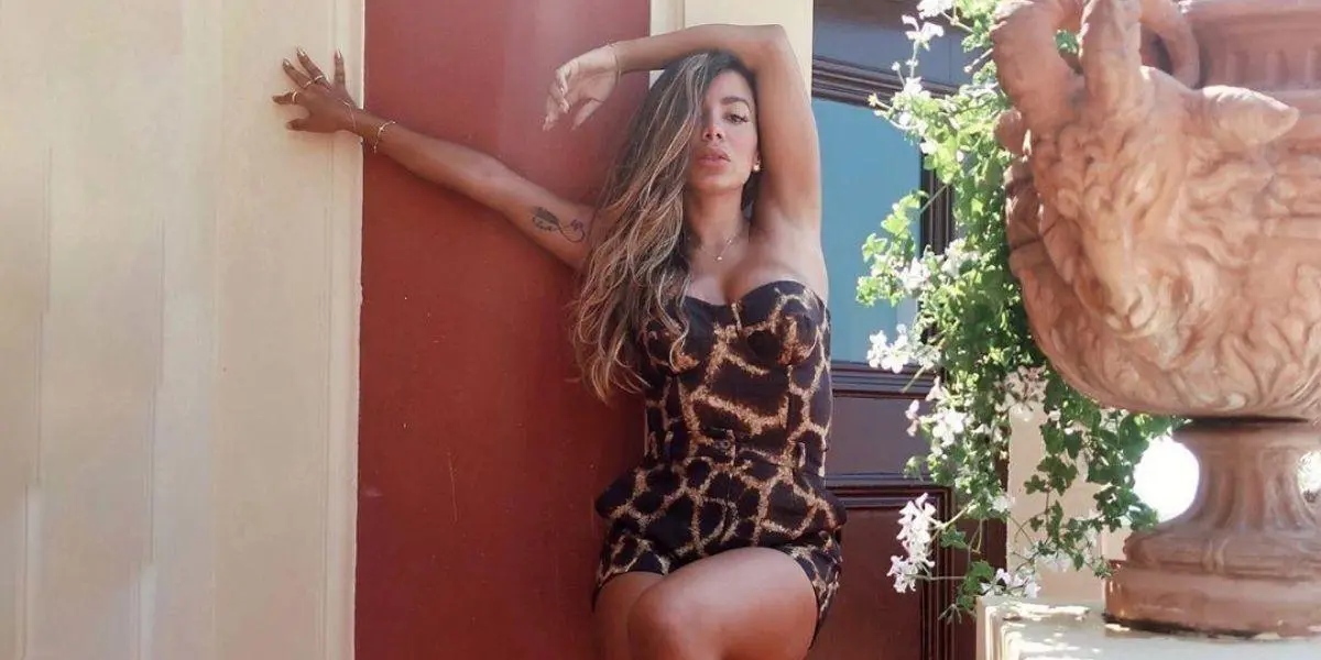 Anitta vestida com estampa animal print posada encontada na parede com a perna direita para cima