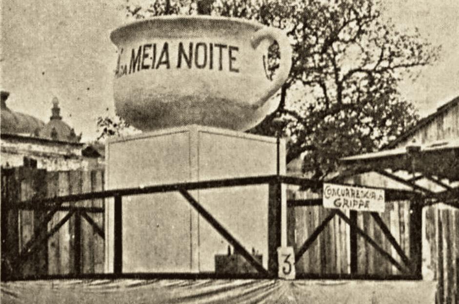 Foto do carnaval de 1929. Uma escola desfila com um xícara grande escrito meia noite.