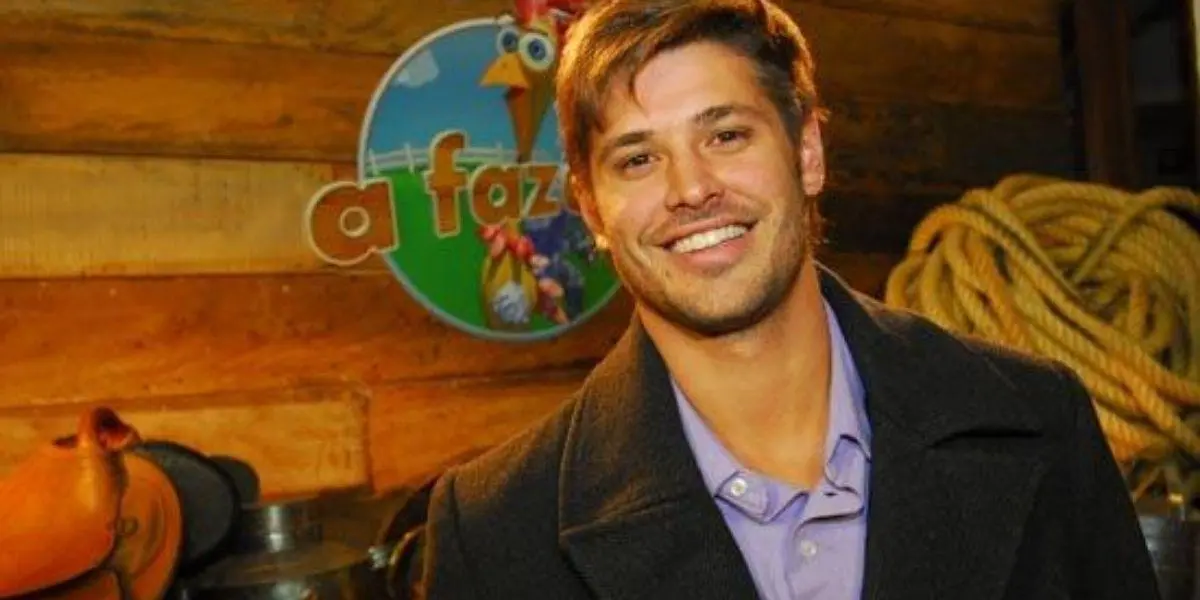 Dado Dolabella posado sorrindo. Atrás dele está o logotipo de "A Fazenda"