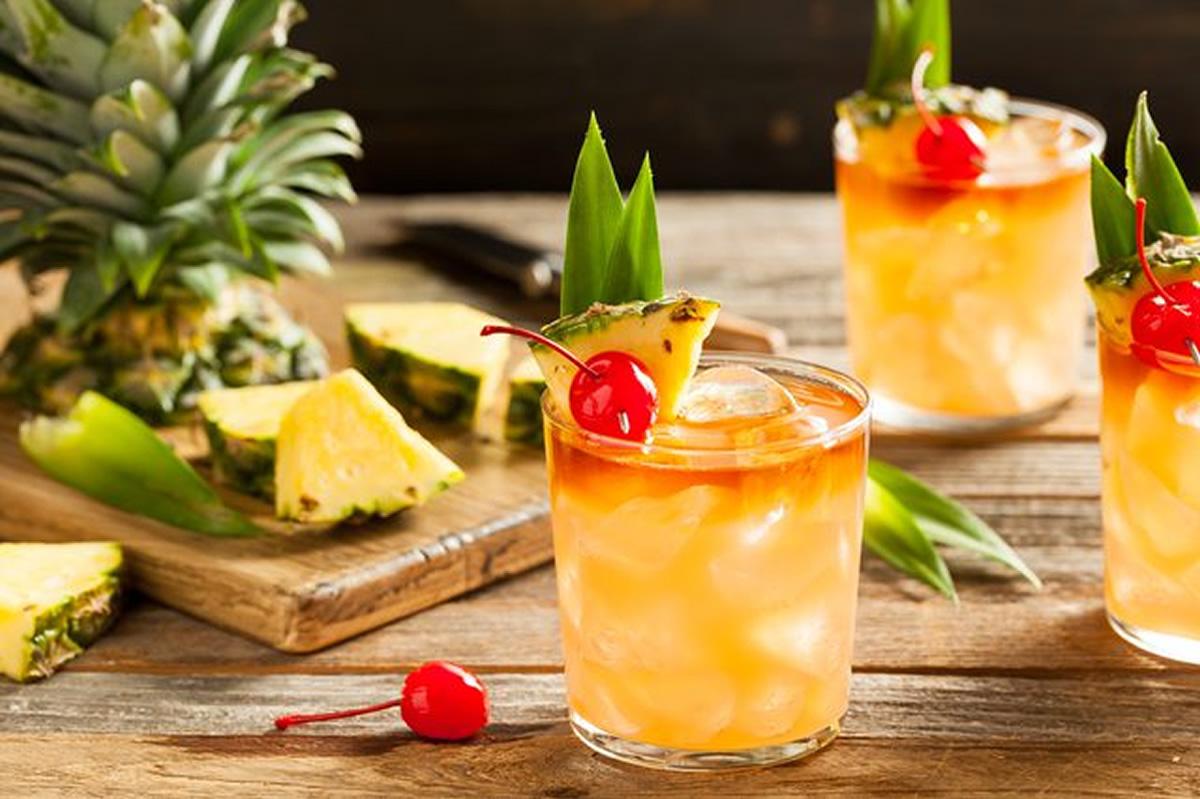 Foto mostra copos com drinks, ao lado de um abacaxi picado.