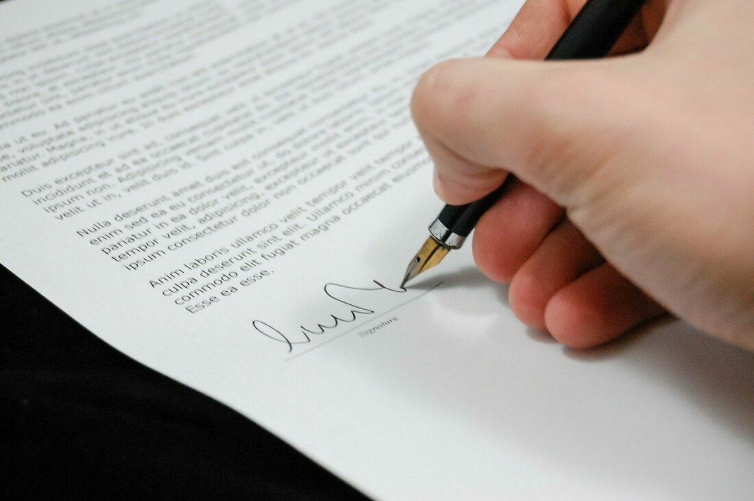 Mão com uma caneta assinando um documento