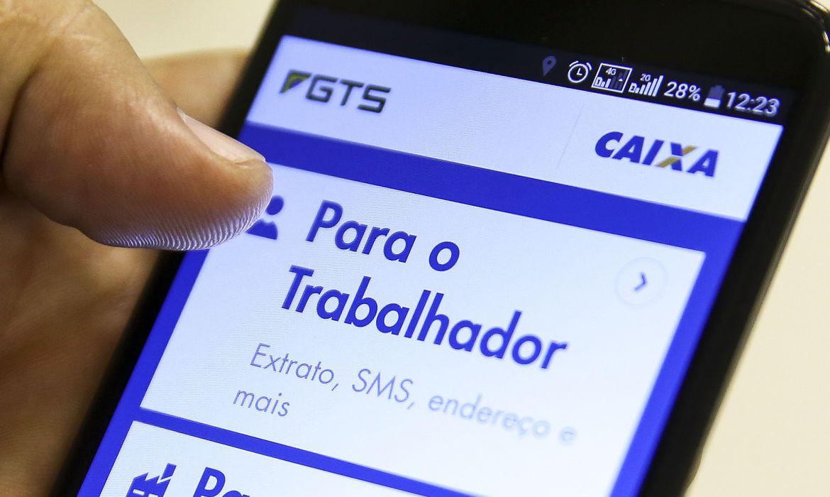 Imagem de mãos segurando o celular aberto no aplicativo FGTS da Caixa Econômica Federal