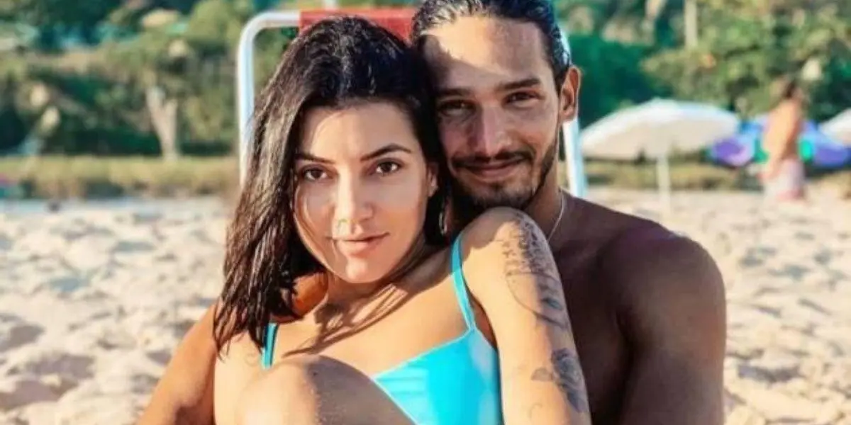 Gabi Prado e João Zoli sentados na praia olhando para frente