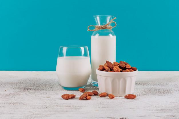 Garrafa de leite com copo de leite e tigela de amendoas vista lateral sobre um fundo branco de madeira e azul 176474 4591