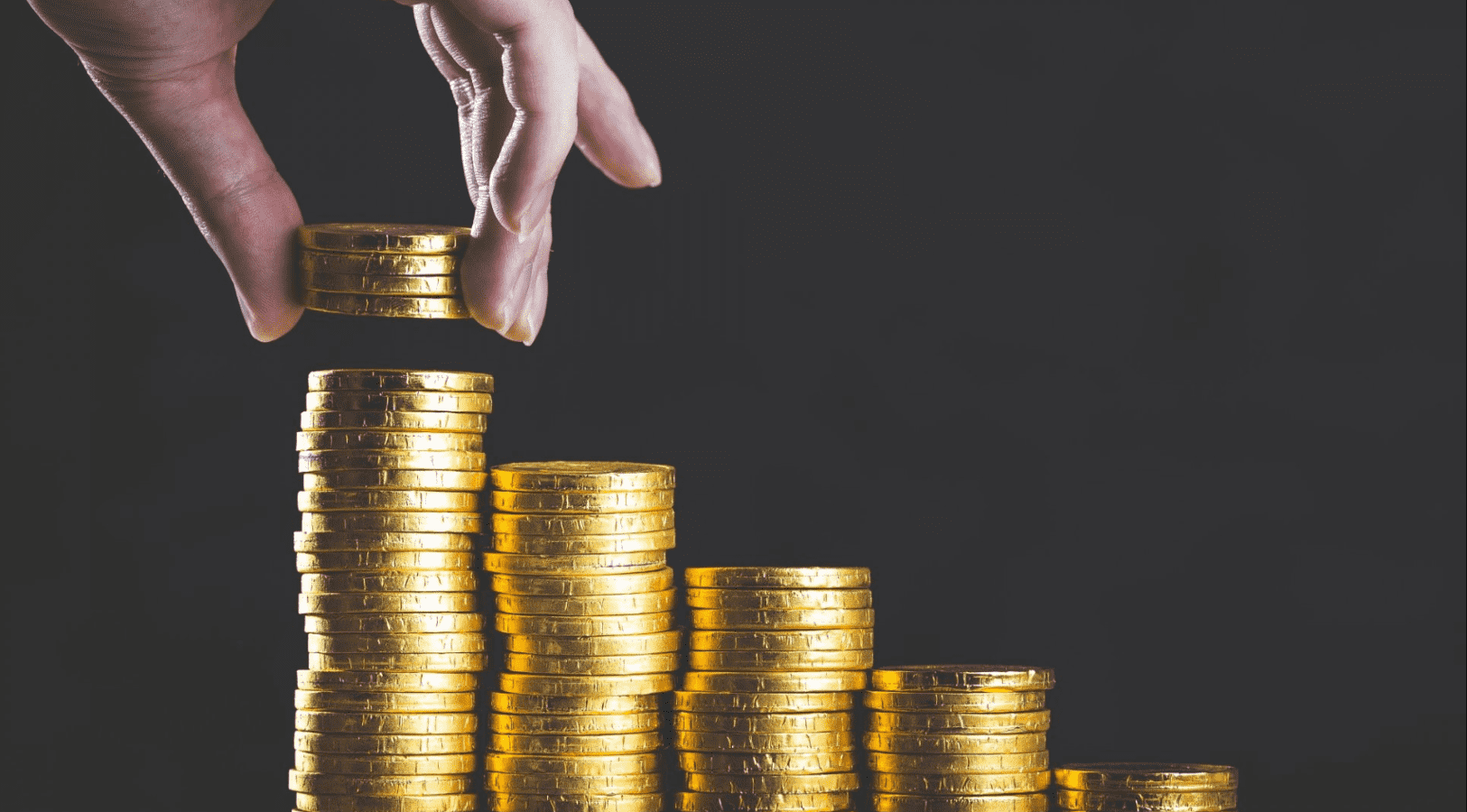 Selic: guia completo de como a taxa influencia sua vida e investimentos 1 Imagem mostra ´pilhas de moedas e uma mão acrescentando outras.