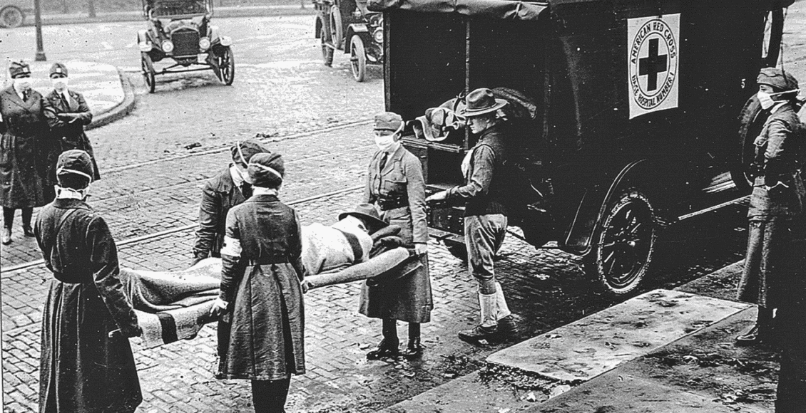 Foto antiga mostra soldados carregando outro soldado em uma maca para o colocar em uma ambulância.