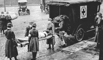 Foto antiga mostra soldados carregando outro soldado em uma maca para o colocar em uma ambulância.