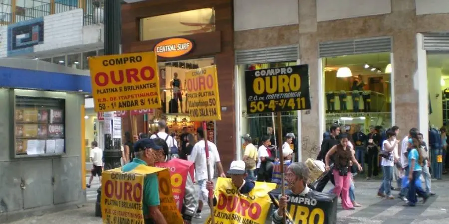 pessoas segurando placa de compro ouro em rua comercial