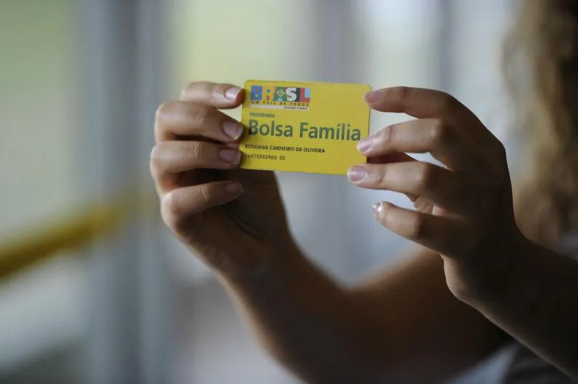 Duas mãos de mulher segurando o cartão do Bolsa Família