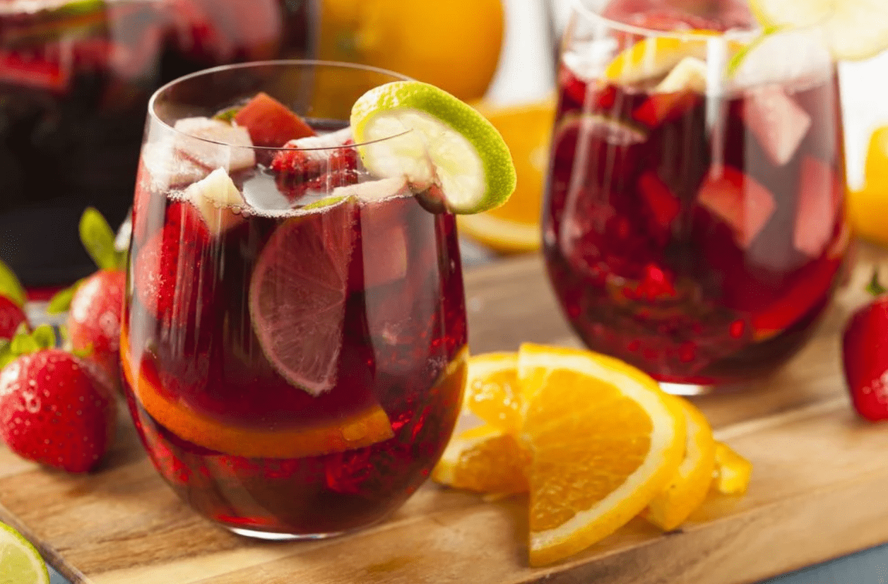 Foto mostra dois copos com sangria em cima de uma tábua. Ao lado de frutas picadas.