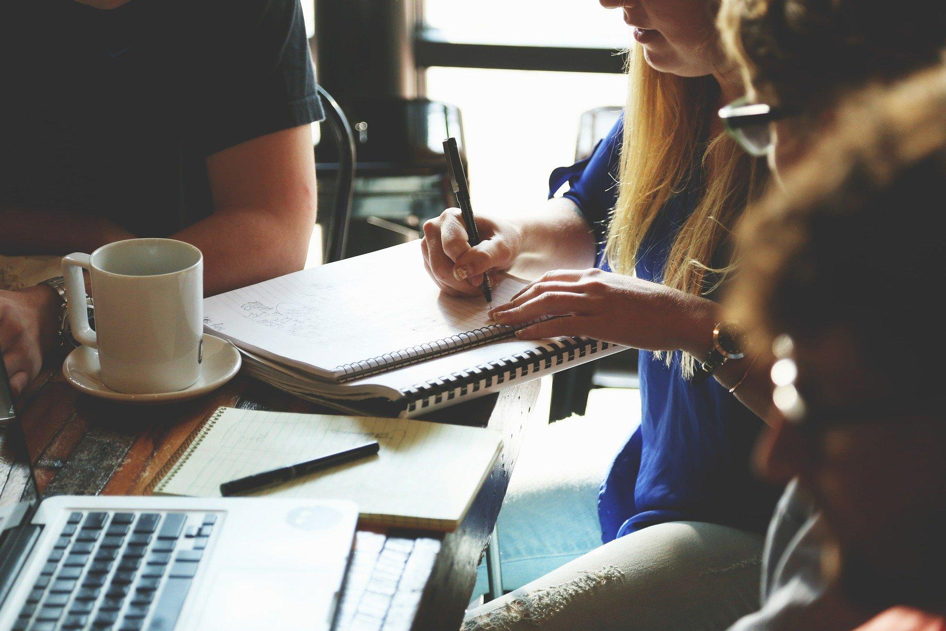 Pessoas em reunião. Mesa com papeis, notebook e copos.