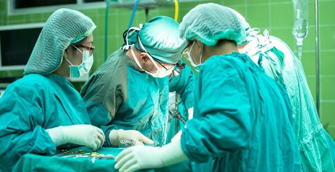 Três médicos com roupa azul com instrumentos médico operando um indivíduo
