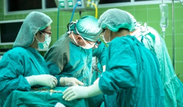 Três médicos com roupa azul com instrumentos médico operando um indivíduo