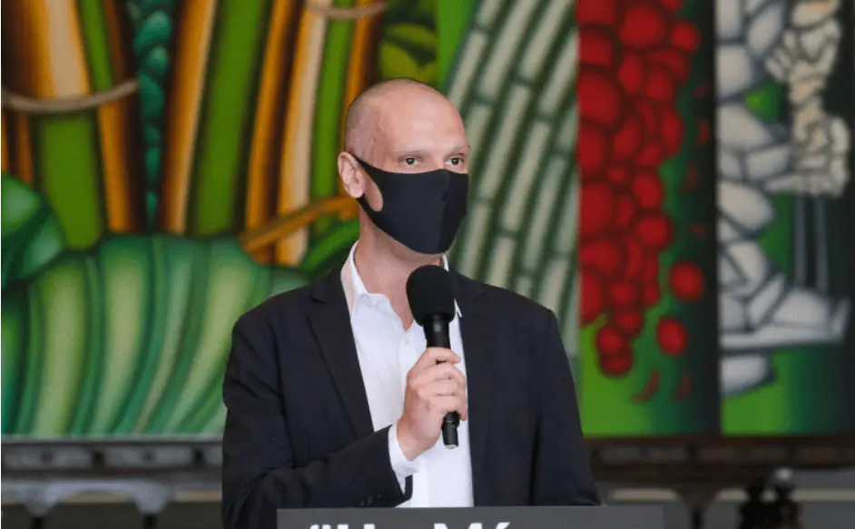 Foto mostra Bruno Covas de máscara falando ao microfone