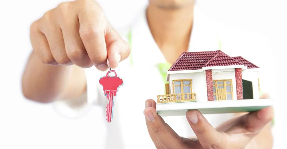 pessoa segurando chave e miniatura de casa