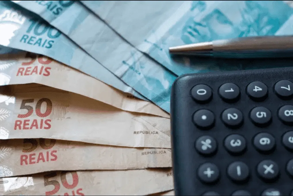 Foto mostra uma calculadora em cima de notas de dinheiro.