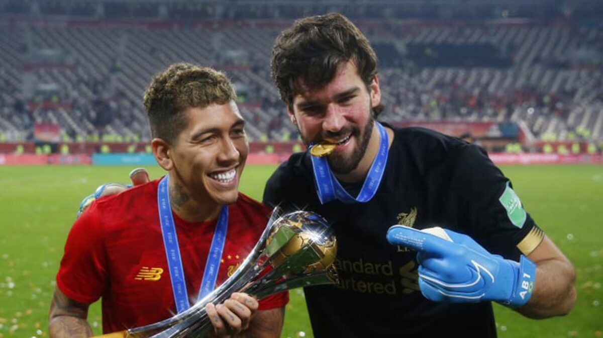 Firmino e Alisson seguram o troféu do Mundial de Clubes conquistado pelo Liverpool; edição de 2020 está incerta